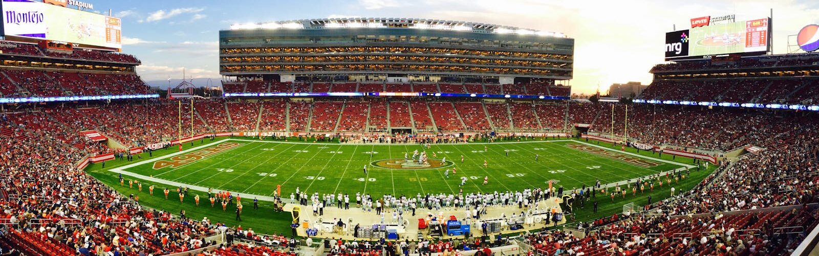 A stunning panoramic shot of Levi's Stadium in Santa Clara during a packed football game at sunset.