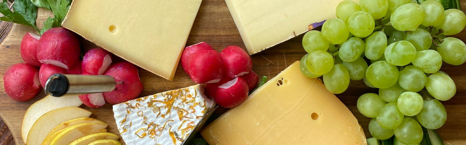 a wooden cutting board topped with cheese and fruit
